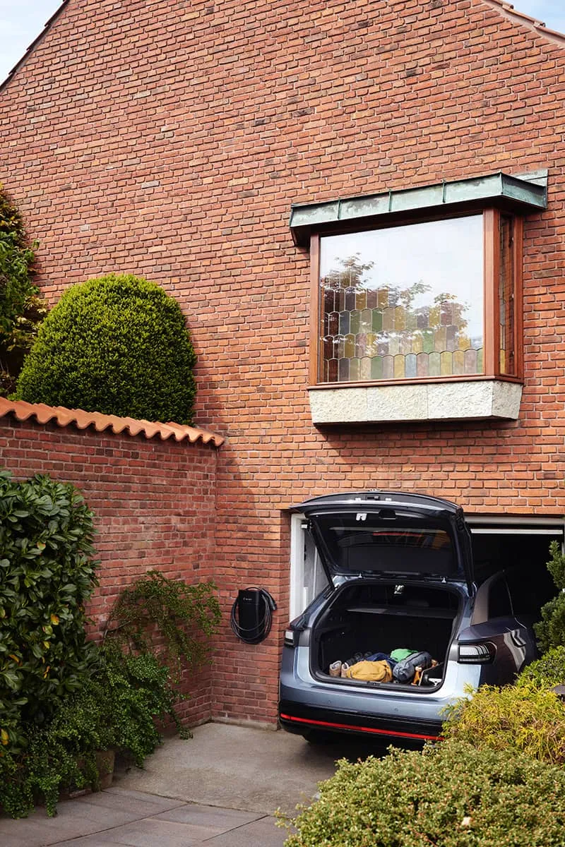 Bil holder opladet i carport, hvor der hænger en sort Clever ladeboks på muren