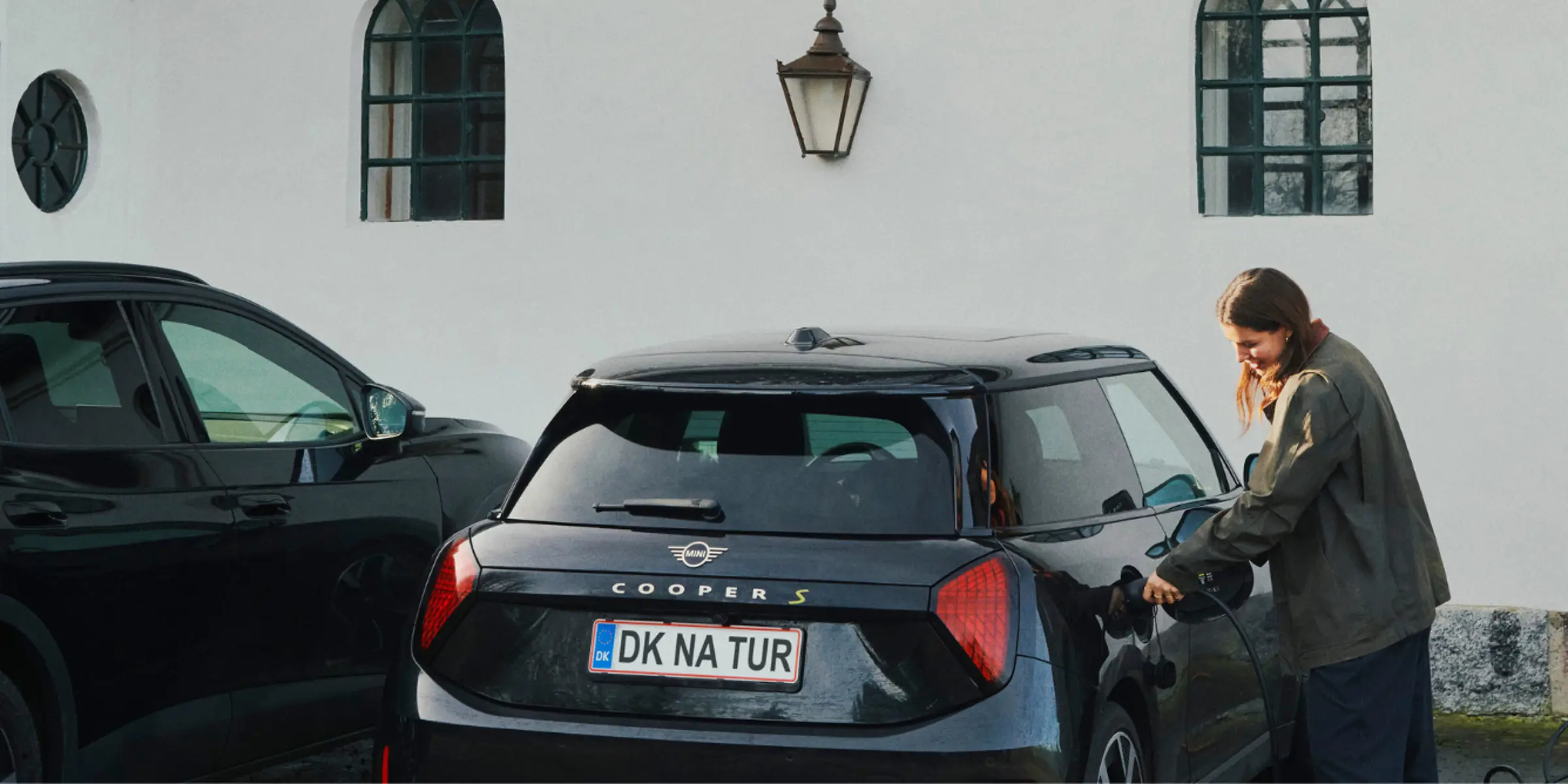Kvinde lader elbil op med to biler parkeret